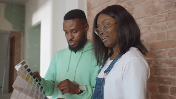 Young African Couple Looking at Color Samples at Home Choosing Paint for Wall