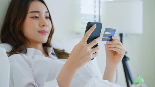 Asian attractive woman  holding credit card enjoy shopping online on bed at home in morning.