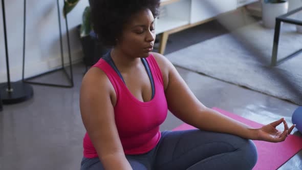 African american female plus size sitting on exercise mat meditating