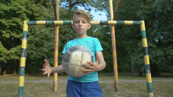 Serious Boy With Football Looking Into Camera at Football Pitch, Street Match