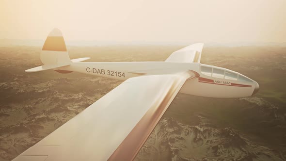 The white sailplane calmly gliding in the sky over the snow-covered mountains.