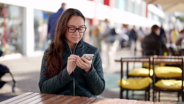 Adult Brunette Woman with Smartphone is Sitting in Street Cafe Chatting in Application in Phone