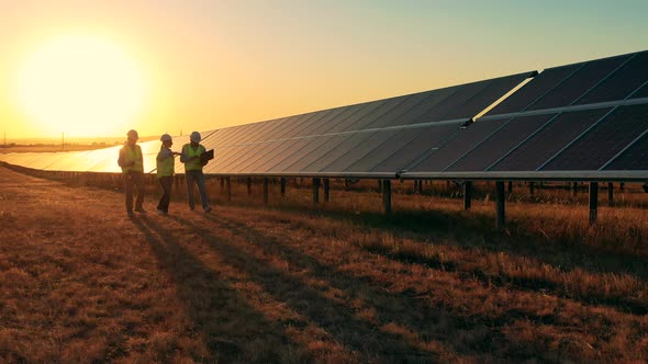 Three Solar Energy Specialists Walking Through a Solar Park at Sunset