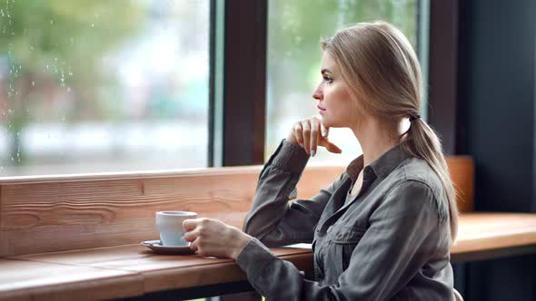 Beautiful Pensive Blonde Unhappy Woman Looking Out of Window at Rainy Autumn Day Sitting in Cafe