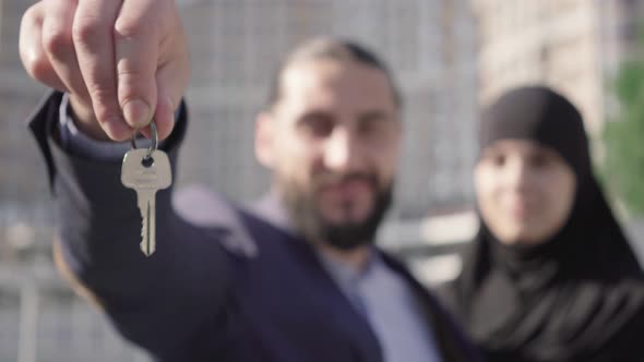 Close-up of Key in Male Hand with Blurred Middle Eastern Couple Smiling at the Background. Happy
