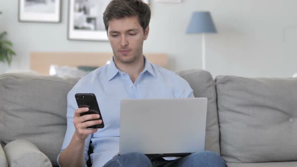 Handsome Young Man Using Smartphone for Work Sitting on Couch