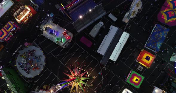 Aerial birds eye dolly forward shot of carnival/fair and rides at night.