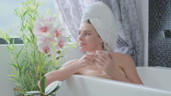 Joyful  millenial woman in a towel on her head with eyes closed taking a hot bath