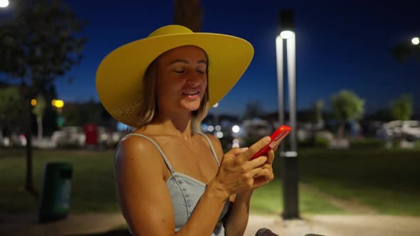 Beautiful Young Woman in a Dress and Hat Walks in the Evening City