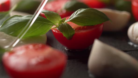 Camera follows pouring olive oil over tomato and mozzarella cheese salad. Slow Motion.