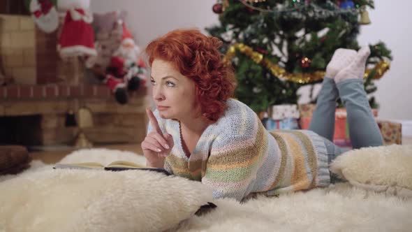 Thoughtful Redhead Caucasian Woman Reading Book at Home on Christmas Eve