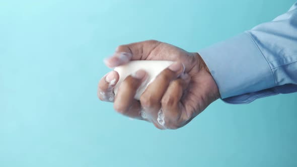 Young Man Washing Hands with a Soap Against Blue Background