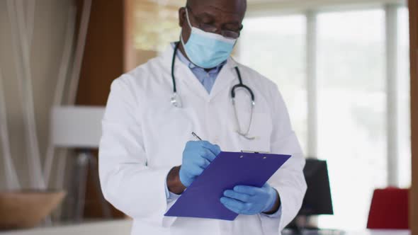 African american senior male doctor wearing white coat writing in notebook