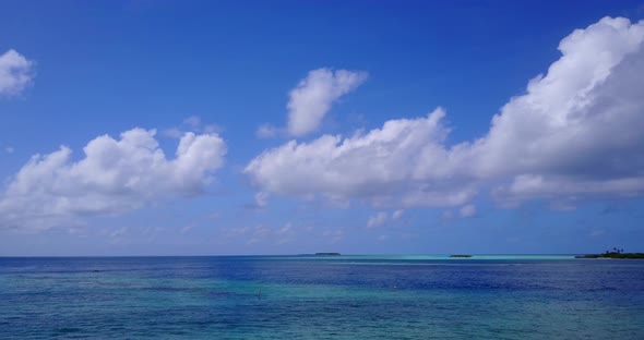 Wide angle fly over island view of a white sandy paradise beach and blue sea background in vibrant 4