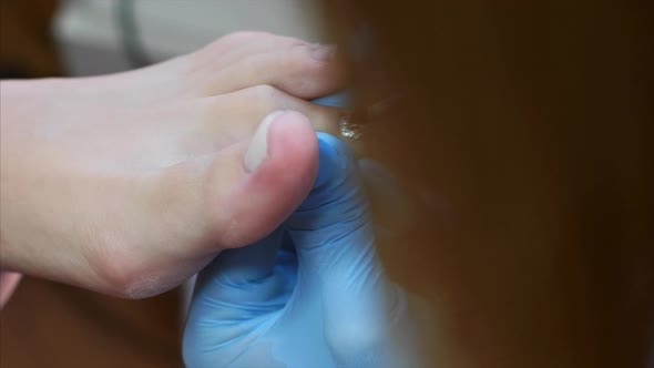 Pedicure Master in Gloves Paints Toenails Using Silver Glitters in Beauty Salon