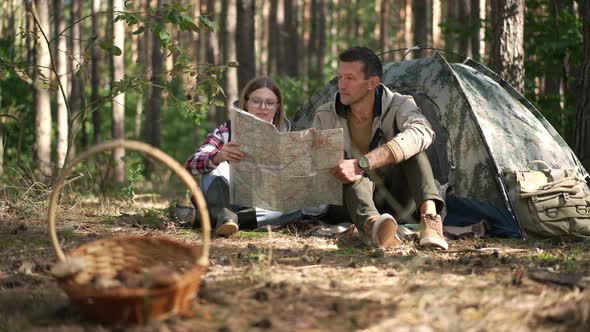 Wide Shot Happy Couple Talking Examining Paper Map Sitting in Forest at Camp Tent