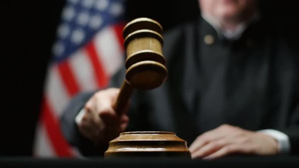 Judge With Wooden Hammer In His Hand Against American Flag In USA Court Room