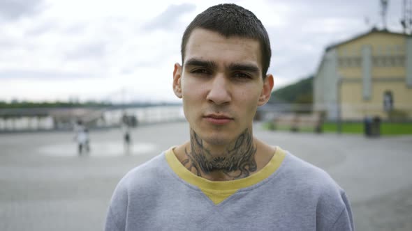 Portrait of a Young Man with a Tattoo on His Neck Standing Against the Sky with Clouds