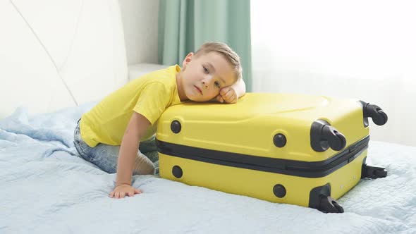 Small Boy Is Waiting for a Vacation Sitting Next To a Yellow Suitcase