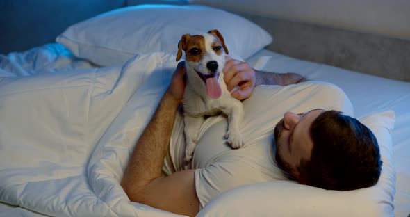 a Man Is Lying on a Sofa with White Bed Linen with His Dog. the Guy Holds the Animal on His Stomach