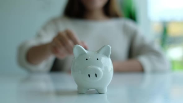Closeup of a woman putting coin into piggy bank for saving money and financial concept