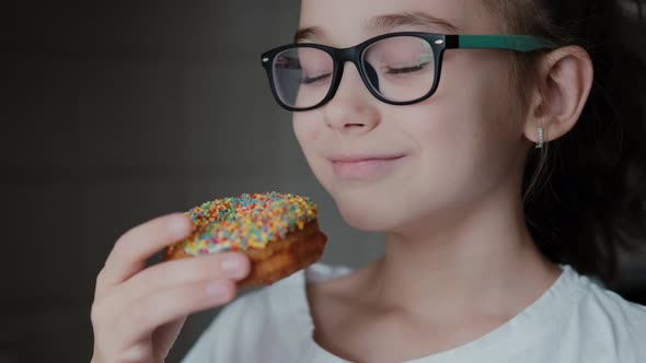Cute Little Girl with Glasses Loves Sweet Donuts. Smiling Female Child Looks at Food Close-up
