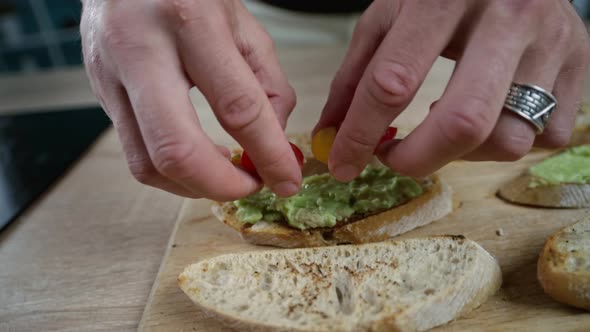 Hand Puts Cherry Tomatoes on an Avocado Sandwich