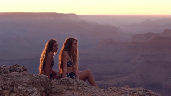 Twin teenage sisters overlooking canyon as one helps the other to stand up