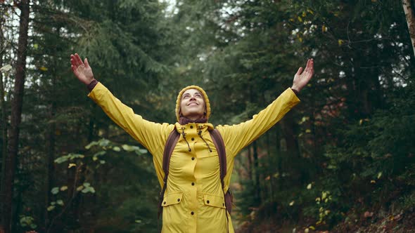 Portrait of Inspired Young Pretty Woman Hiker with Backpack Wearing Bright Yellow Raincoat and