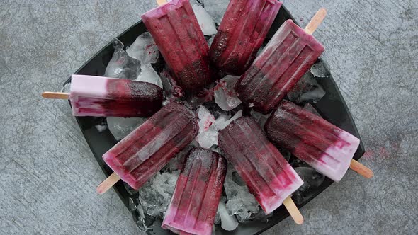 Homemade Fresh Frozen Blueberry and Blackberry Popsicles on Black Plate with Ice Sitting on Stone