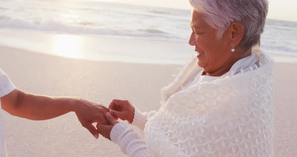 Happy hispanic senior woman putting ring on man hand on beach at sunset