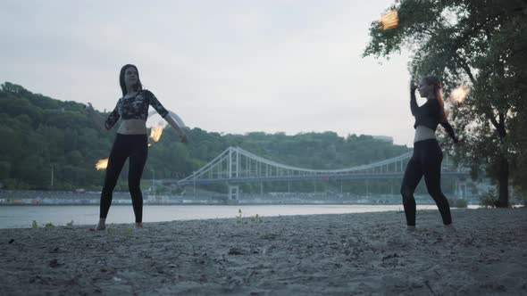 Two Young Women Performing a Show with Flame Balls Standing on the Riverbank. Skillful Fireshow