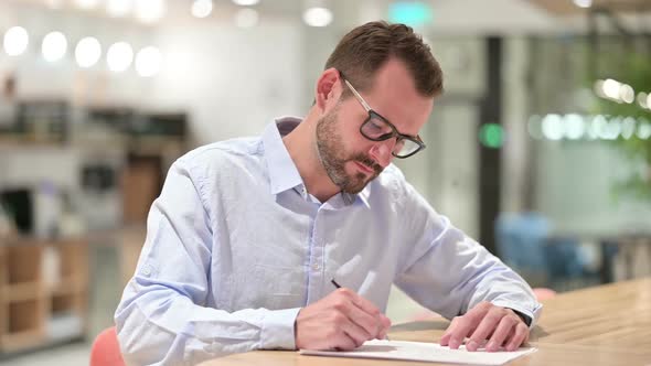 Serious Businessman Writing on Paper in Office