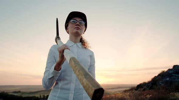 Woman Dressed Office Clothes in Helmet and with Pickaxe on Shoulder Walks Forward Against Background