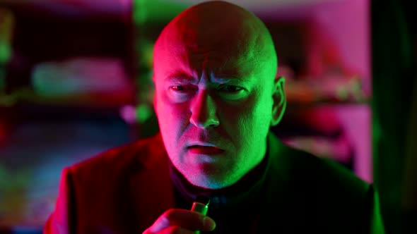 Middleaged Bald Man is Smoking Ecigarette in Nightclub Male Portrait in Flashing Neon Lights