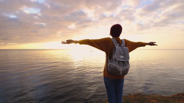 Young GoodLooking Woman Wearing Red Hat and Yellow Sweater and Slowly Approaching Ocean