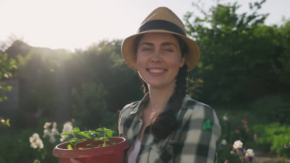 A young woman picks up a pot of plants and smiles. Real time. Jib shot. Earth Day Concept.