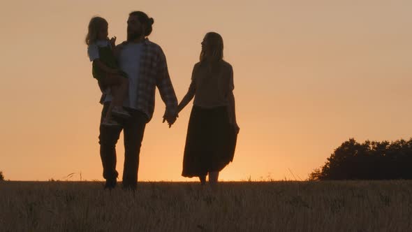 Young Family of Farmers Silhouettes of Three People Parents with Child Walking on Wheat Field in