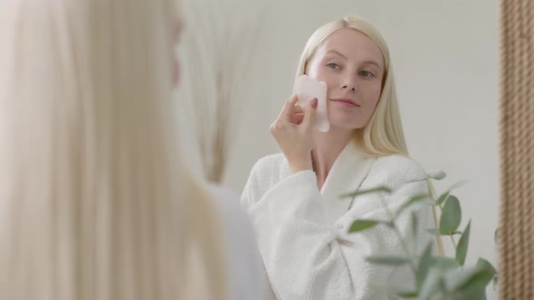 Pretty Female Doing Facial Massage in Bright Bathroom