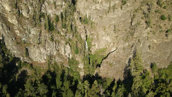 Aerial dolly out of Corbata Blanca thin waterfall falling between mountains with pine trees, Patagon