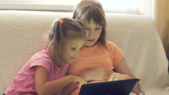 Two Girls Children Sister At Home On Couch Playing On Tablet