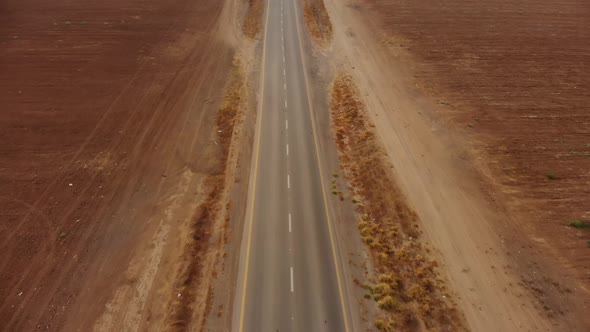 drone aerial shot of the desert's empty road revealing the endless horizon and some cars.