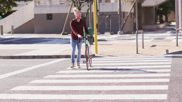 Albino african american man with dreadlocks crossing road with bike