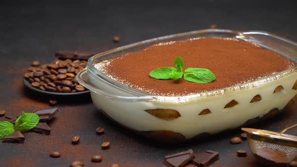 Tiramisu Dessert in Glass Baking Dish and Pieces of Chocolate Bar on Concrete Background