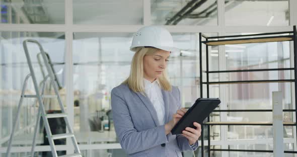 Female Engineer in Hardhat Inspecting New Office Building and Revisioning Plan 