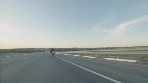 Man in Helmet and Black Shirt is Riding Along the Highway on Cool Motorcycle Back View