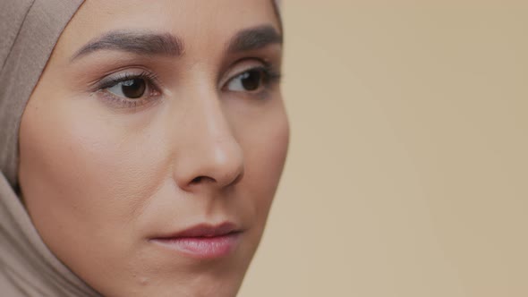 Close Up Portrait of Young Serious Muslim Woman in Traditional Headscarf Looking Aside Beige