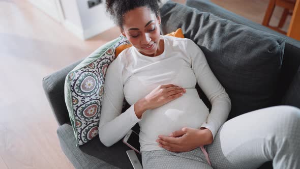 Happy African pregnant woman lying on the couch