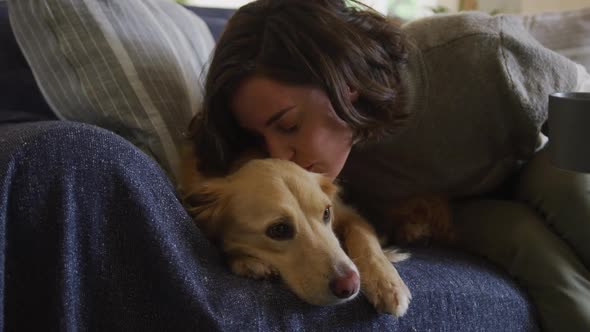 Smiling caucasian woman kissing her pet dog sitting on sofa at home