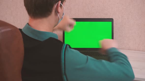 A Man Doing Warm Up Exercises While Sitting at a Laptop Via Video Call in a Protective Face Mask